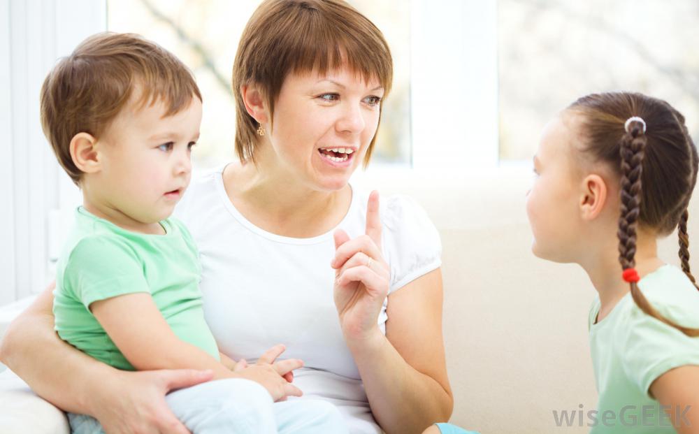woman-in-white-shirt-talking-to-little-girl-in-green-while-holding-boy